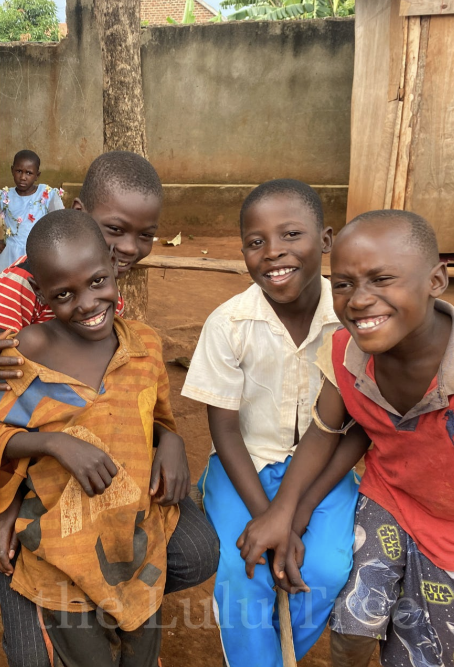 Four boys laughing together in a village courtyard